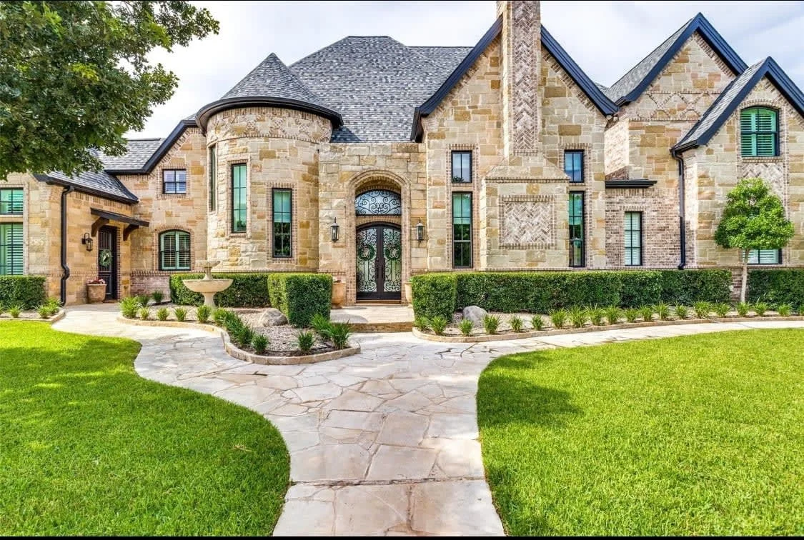 Stone home with a curved entry, pitched roof and landscaped front garden