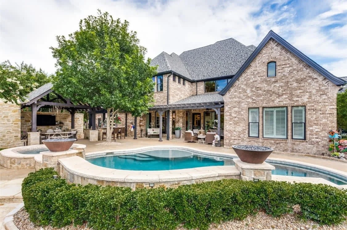 A stone home opening onto a curved swimming pool and outdoor living area